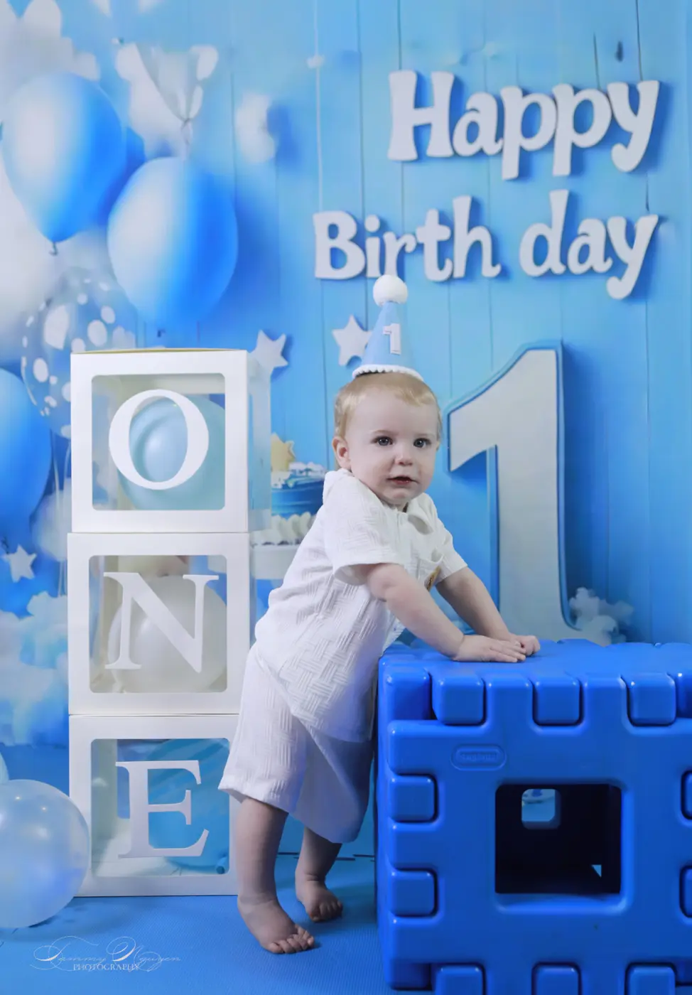 A child standing beside blue first-birthday decorations.
