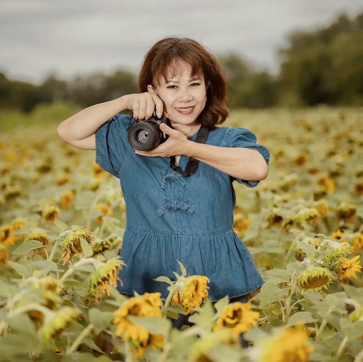 Tammy Nguyen smiling and holding her camera in a sunflower field.