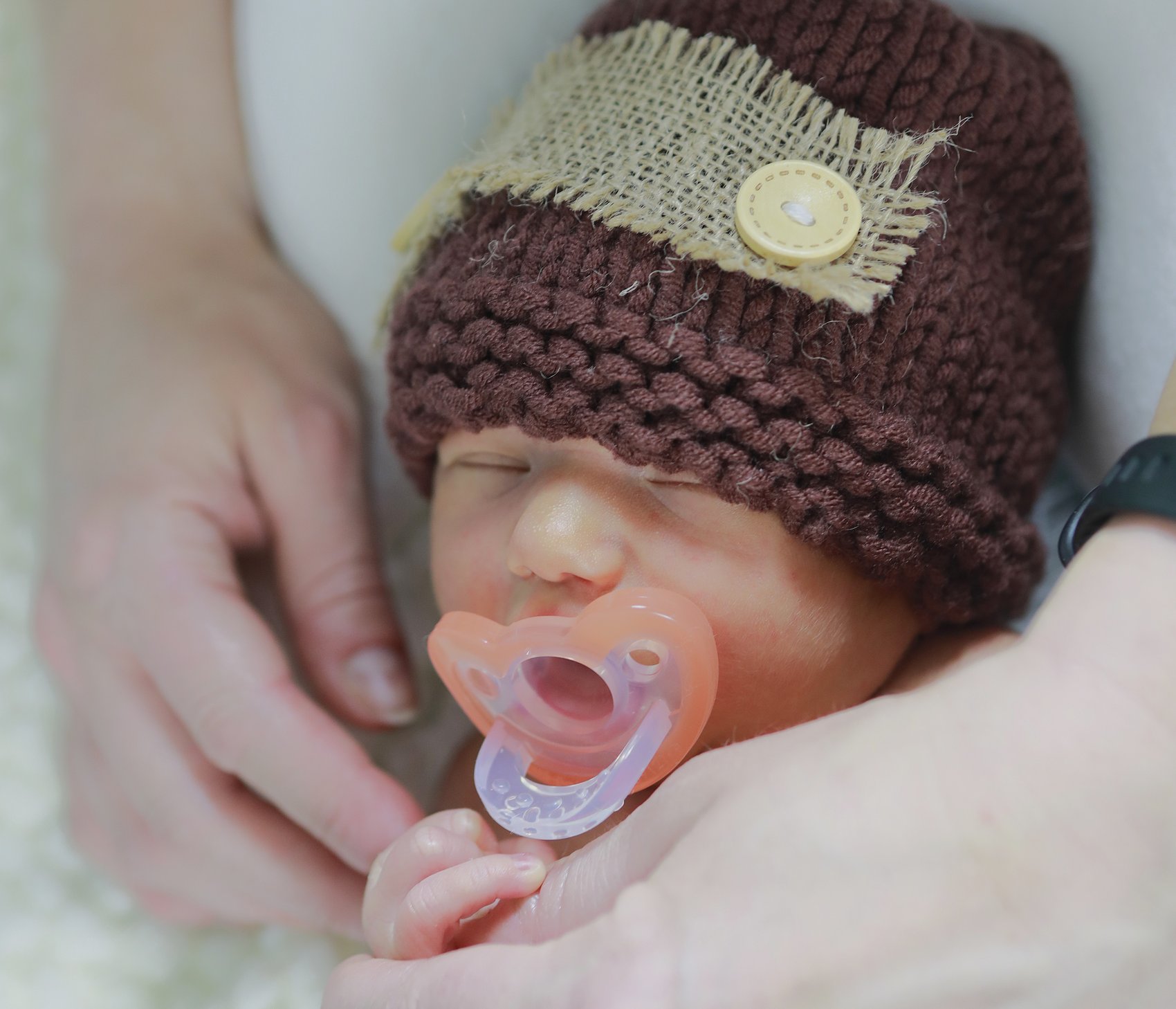 Plate seven: a sleeping newborn in a hand-knit cap, holding a parent's finger.